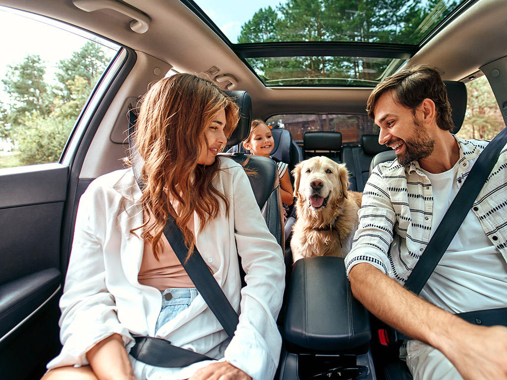 Familie mit Hund sitzt fröhlich im Auto auf dem Weg zum Wander-Urlaub am Hintersee in Ramsau