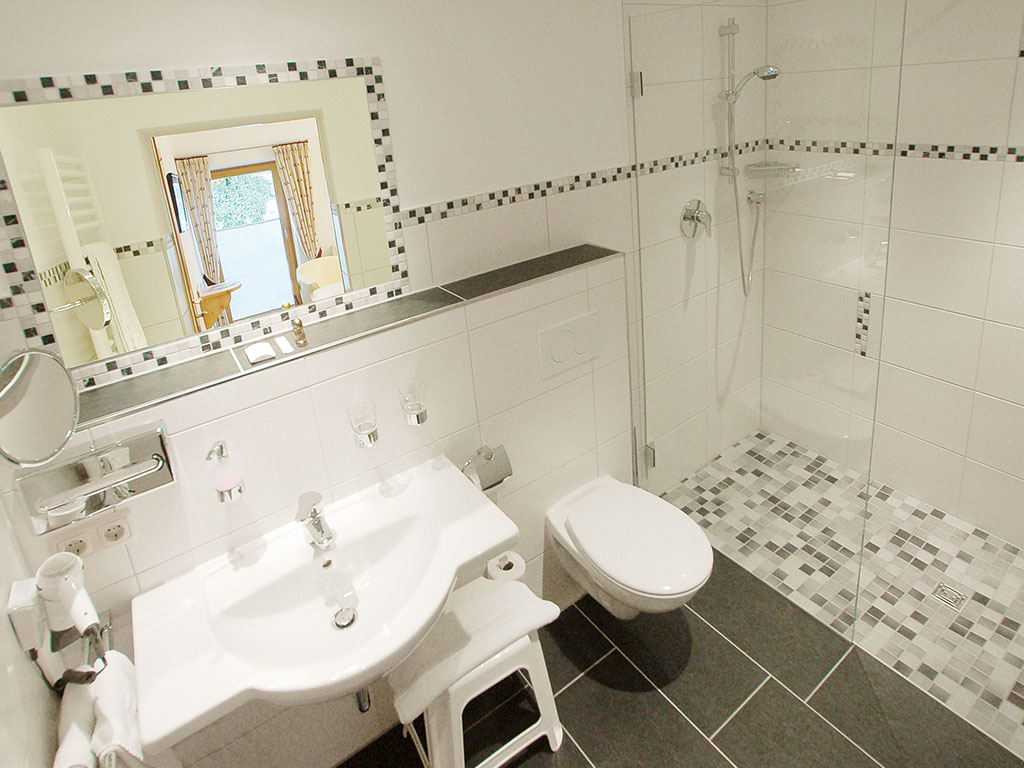 Modernes Badezimmer mit bodengleicher Dusche, Mosaikfliesen, großem Spiegel, Kosmetikspiegel und WC im Wörndlhof Ramsau am Hintersee.