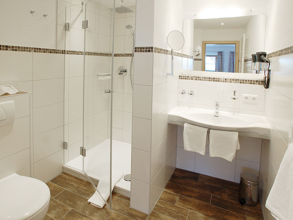 Helles Badezimmer mit Glasdusche, großem Spiegel, Waschbecken, WC und stilvollen Mosaikfliesen im Wörndlhof Ramsau am Hintersee.