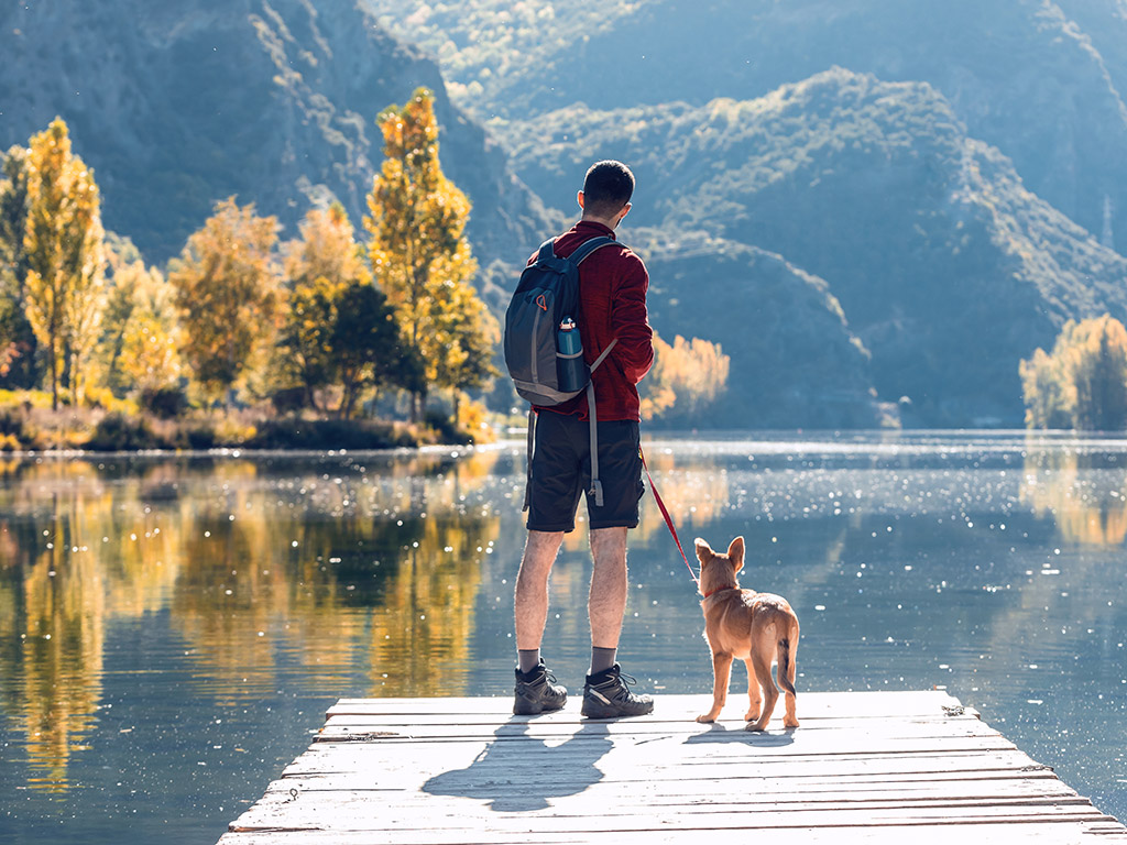Ein Mann mit Hund steht auf einem Holzsteg am Hintersee in Ramsau – Wanderpause mit Blick auf See, Berge und den Zauberwald im Nationalpark Berchtesgaden.